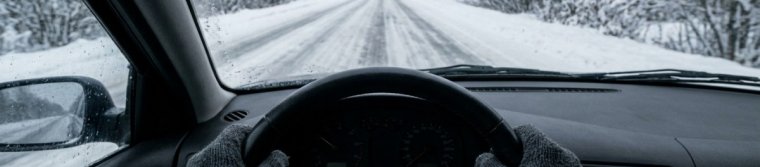Gloved hands on a steering wheel on a snow-covered road