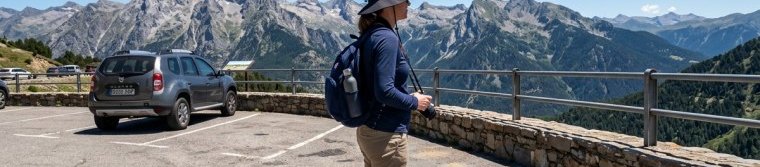 A traveler in a wide-brimmed hat standing at a sunny overlook at midday with a very short shadow